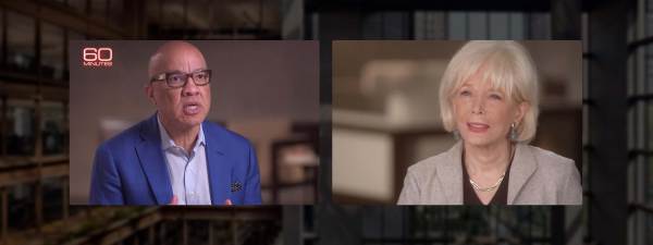 Darren Walker in dark rimmed glasses, a light blue shirt and a bright blue blazer faces Lesley Stahl wearing a black blouse and beige jacket.