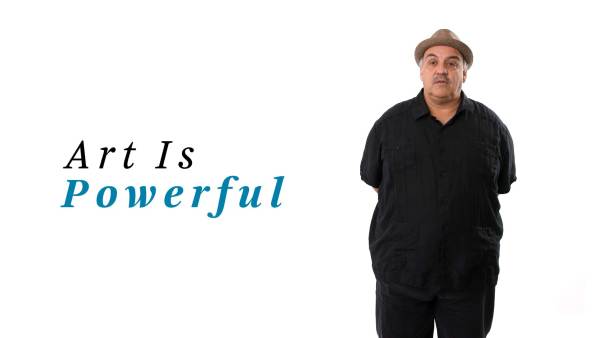 Luis Alfaro wears a straw pork pie hat, a black guayabera shirt, and black slacks. The phrase "Art Is Powerful" appears to the left.