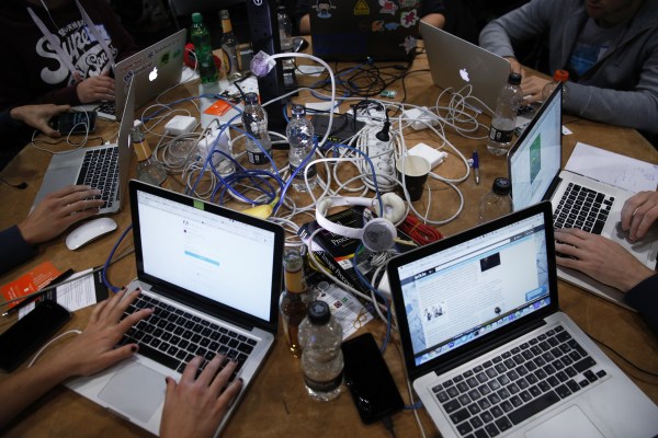 Programmers huddled at a table working on their laptops.