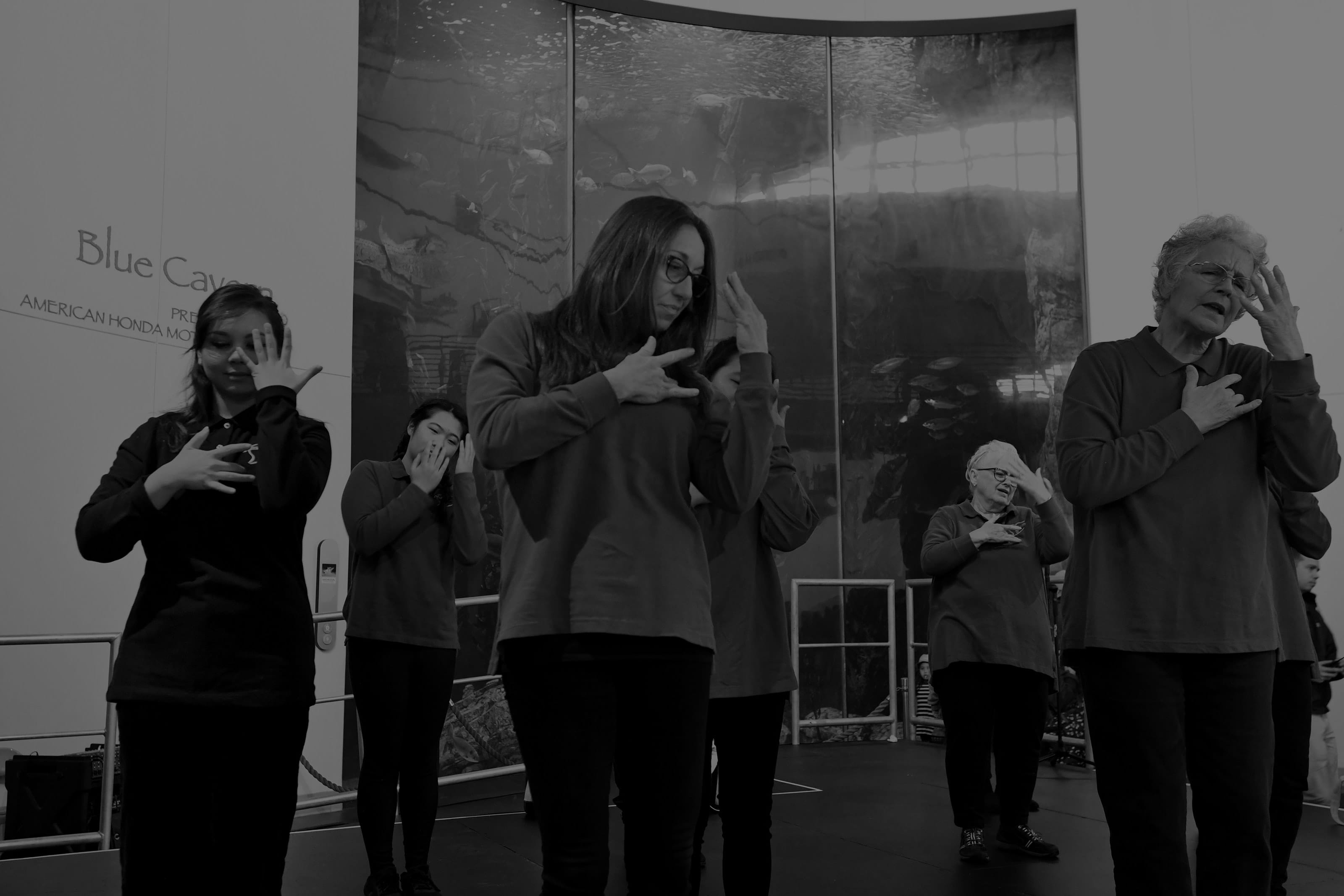 A black and white photo of a group of people performing using sign language.