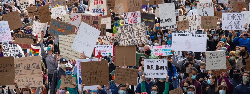 A crowd of people wearing protective masks and holding signs protesting racism and police brutality.