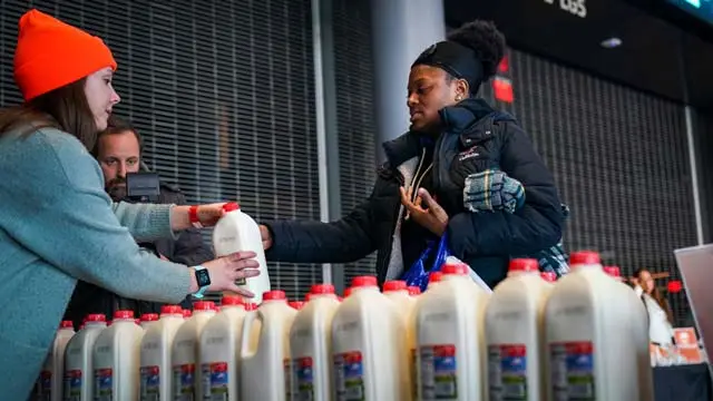 A woman wearing a black coat receives a carton of milk at a food distribution center for federal workers impacted by the government shutdown, at the Barclays Center, in the Brooklyn borough of New York City.